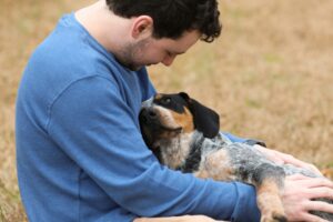 homme assis tenant tendrement son chien dans ses bras